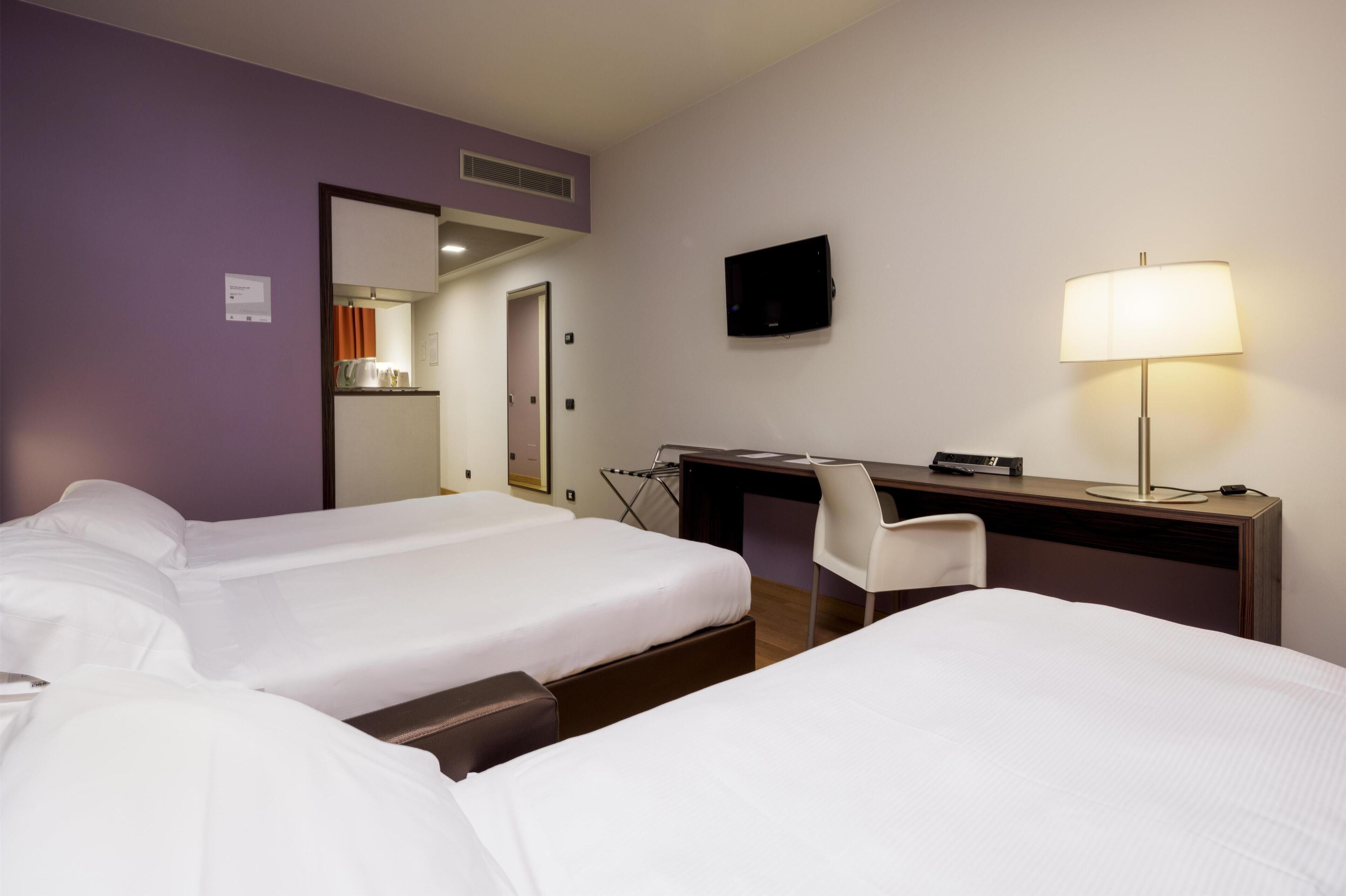 Una habitación de hotel con dos camas, un escritorio, una silla, un televisor y una lámpara.