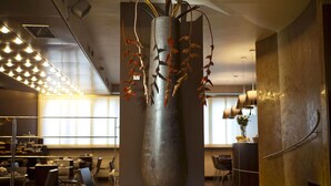 A modern interior with a large metallic vase sculpture, contemporary furniture, and a well-lit dining area. - Hotel Aleramo (Asti)