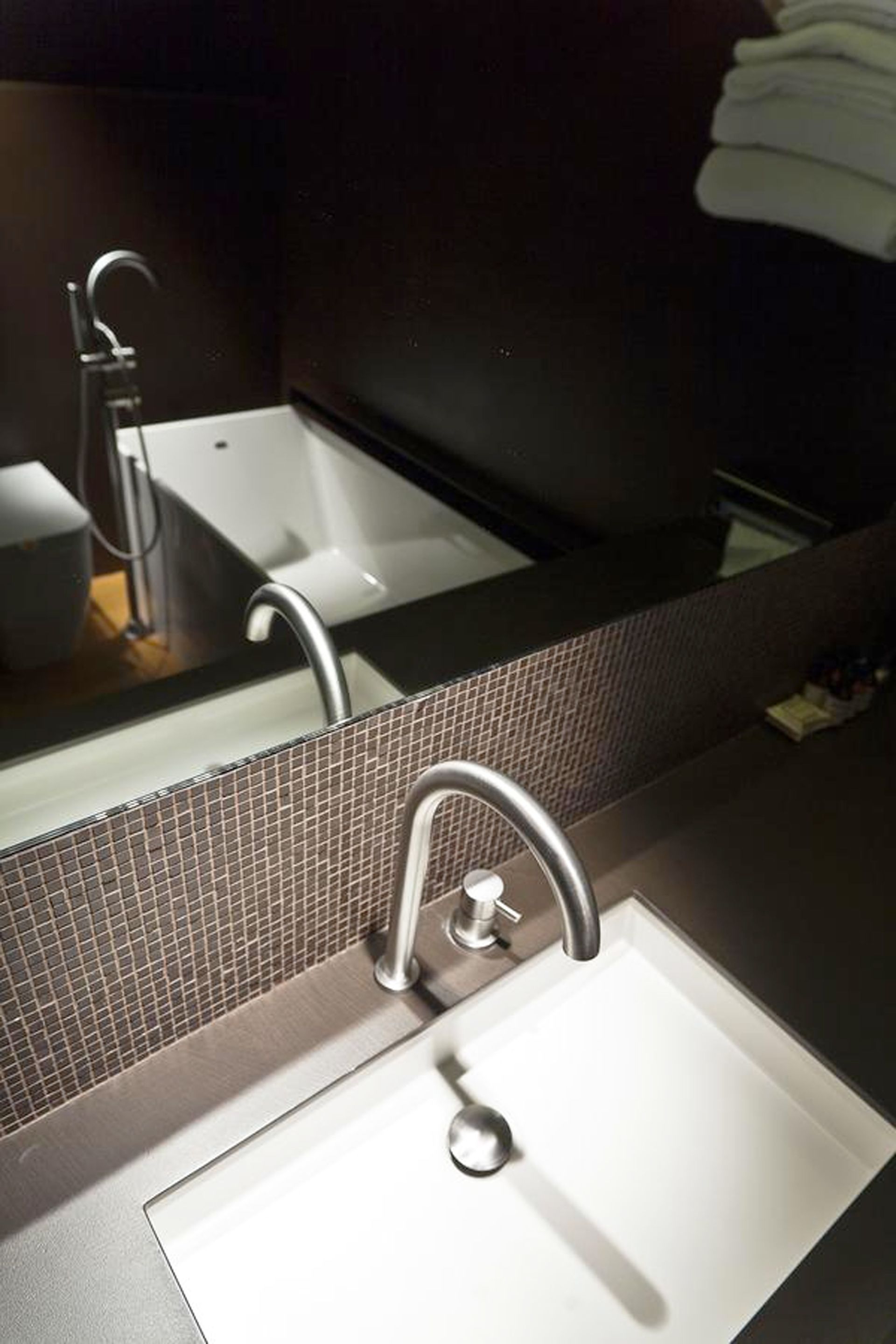 A modern bathroom with a white sink, a chrome faucet, and a large mirror above it.