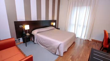 Une chambre d’hôtel avec un lit, une table de chevet, une lampe, une chaise et une fenêtre avec des rideaux.