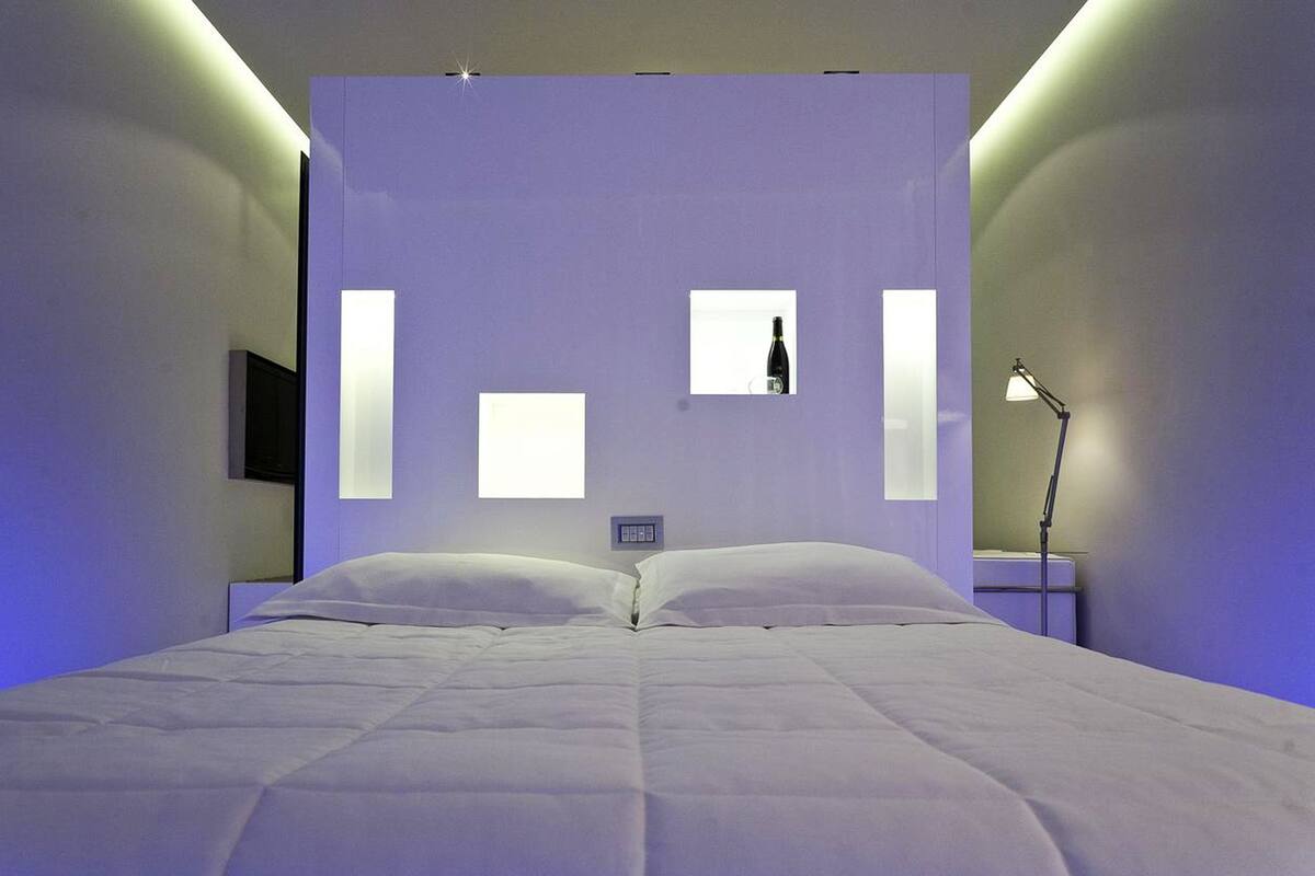 A modern bedroom with a large bed, a nightstand, a lamp, and a wall-mounted TV.