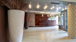 A spacious lobby with a reception desk, large potted plants, and a modern ceiling design. - Hotel Aleramo (Asti)