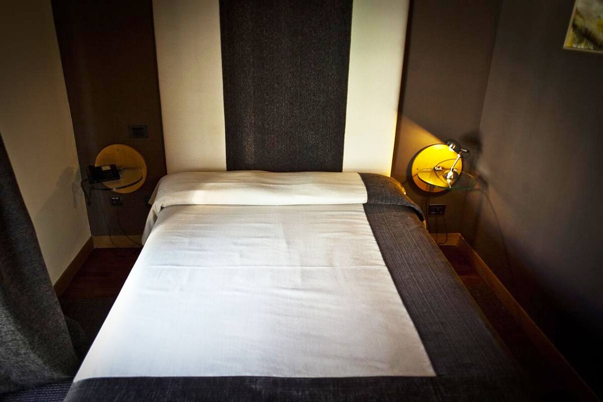 A hotel room with a bed, two bedside tables, and a wall-mounted lamp.