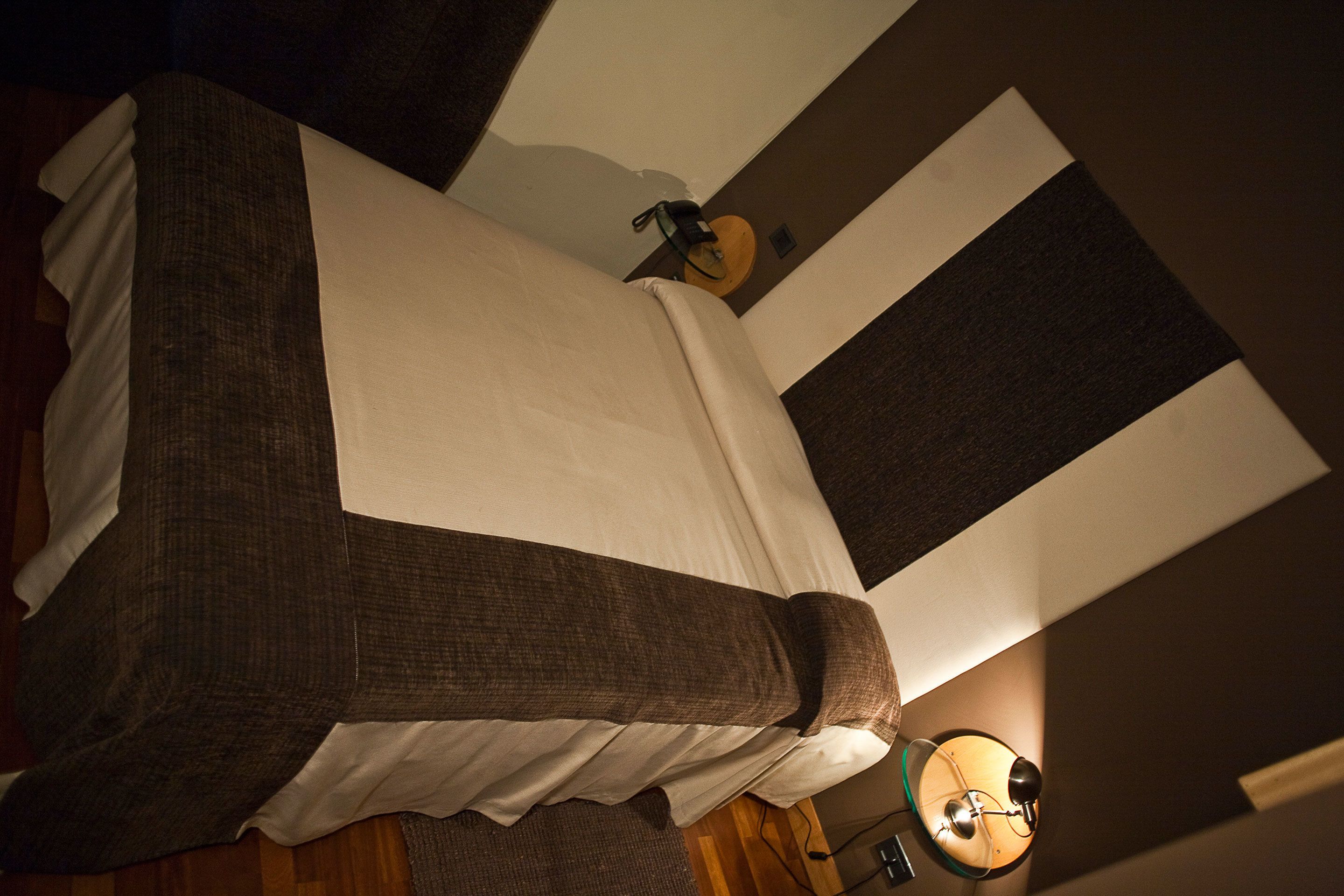 Una cama con un edredón blanco y marrón, una mesita de noche con una lámpara y un reloj de pared.
