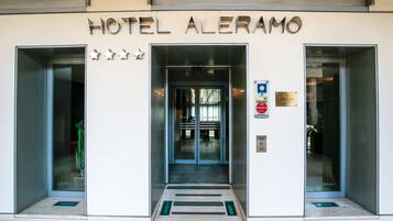 L’entrée de l’hôtel Aleramo présente un design moderne, avec une porte en verre, une enseigne métallique au-dessus de l’entrée et une classification de quatre étoiles.