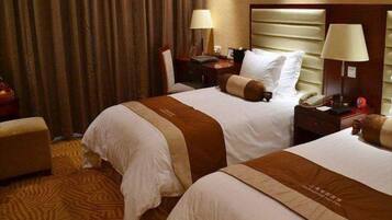 A hotel room with two beds, a nightstand with a lamp, a telephone, and a chair.