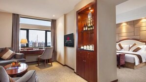 Habitació d'hotel amb una finestra gran, una taula de treball, un llit i un minibar.