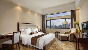 Habitació d'hotel amb un llit gran, un escriptori, una cadira, un televisor i vistes a la ciutat.