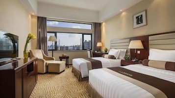 A hotel room with two beds, a desk, a chair, a TV, and a large window with a city view.