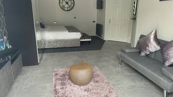 Een moderne woonkamer met een grijze bank, een rond geweven poef en een bed met een grijs hoofdeinde.