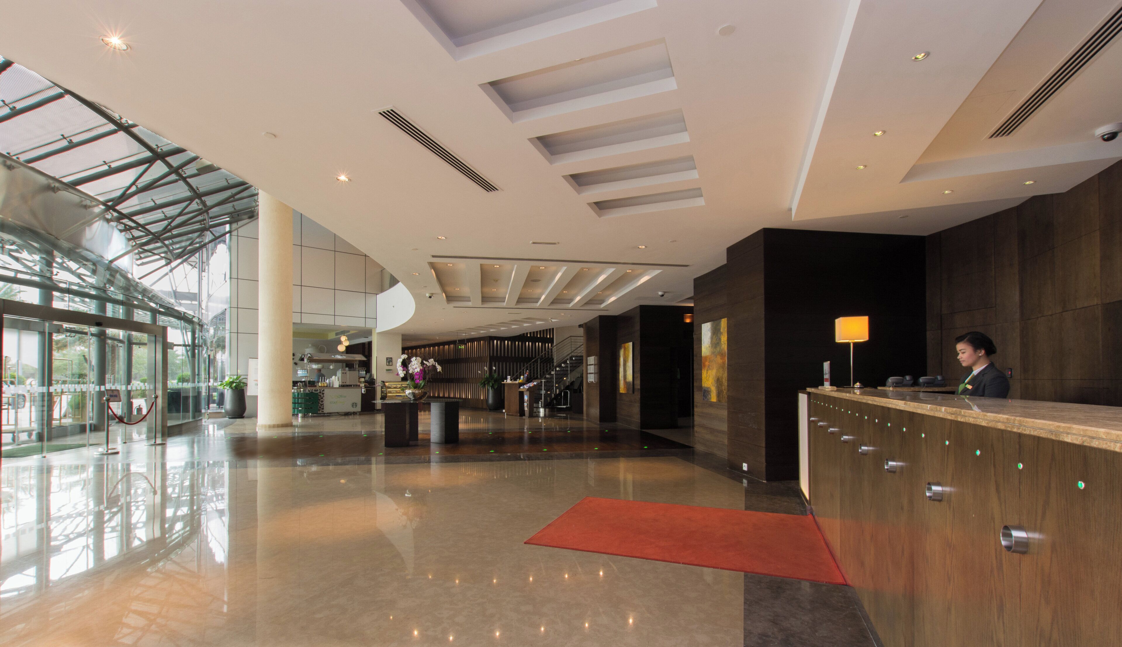 Eine moderne Hotelhalle mit einer Rezeption, einer Treppe und einer Glasfassade.