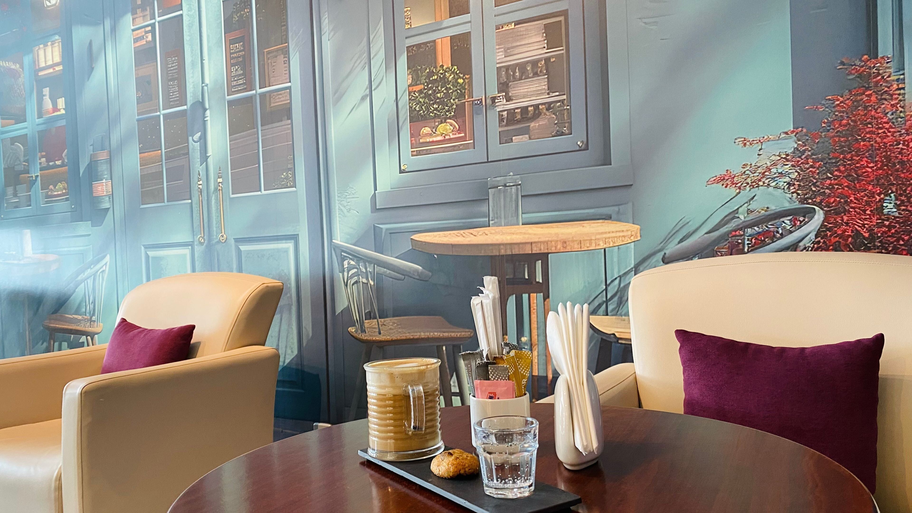 A cozy room with a round table, two chairs, a coffee pot, a glass, and a tray with a cookie.