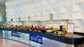 A buffet setup with various food items and condiments, a signboard, and a modern geometric wall design.