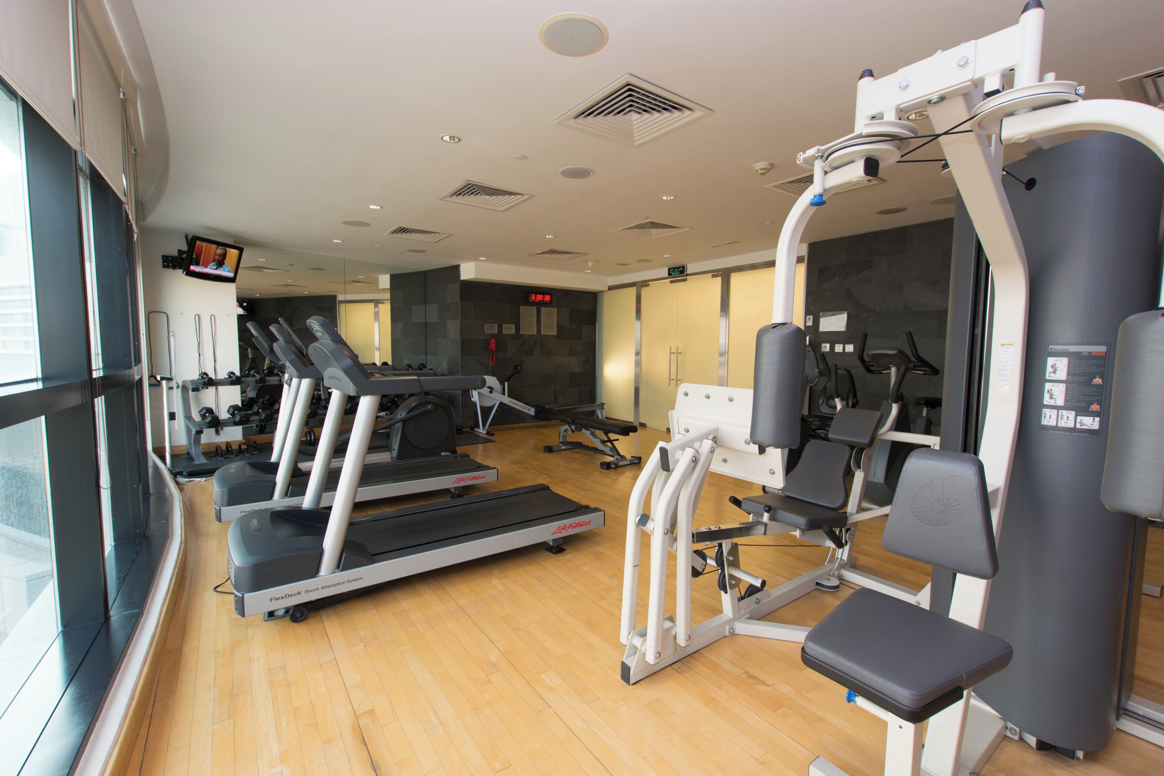 Een fitnessruimte met cardioapparatuur, krachttoestellen en een digitale klok.