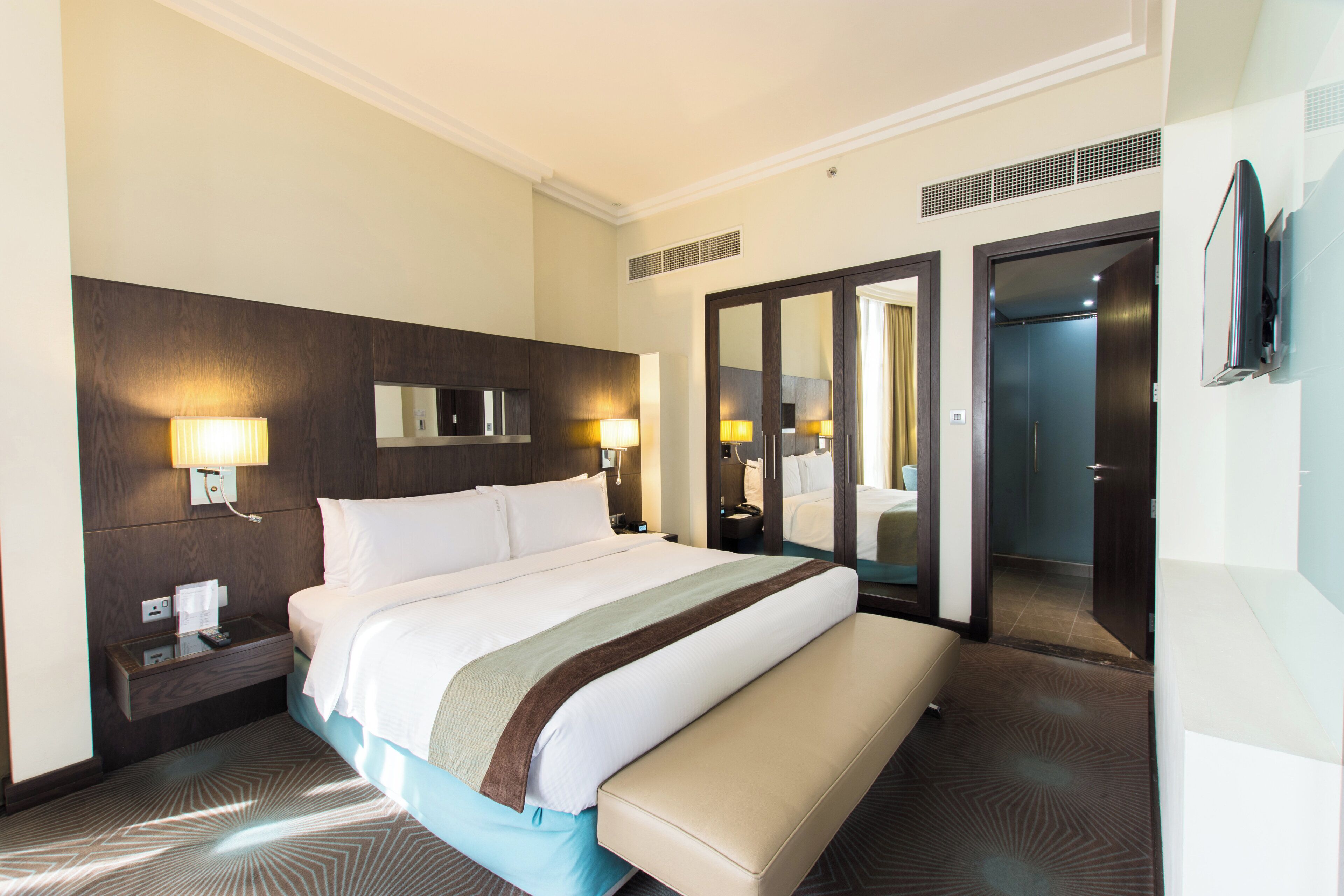 A hotel room with a large bed, bedside lamps, a mirror, a wardrobe, and a television.