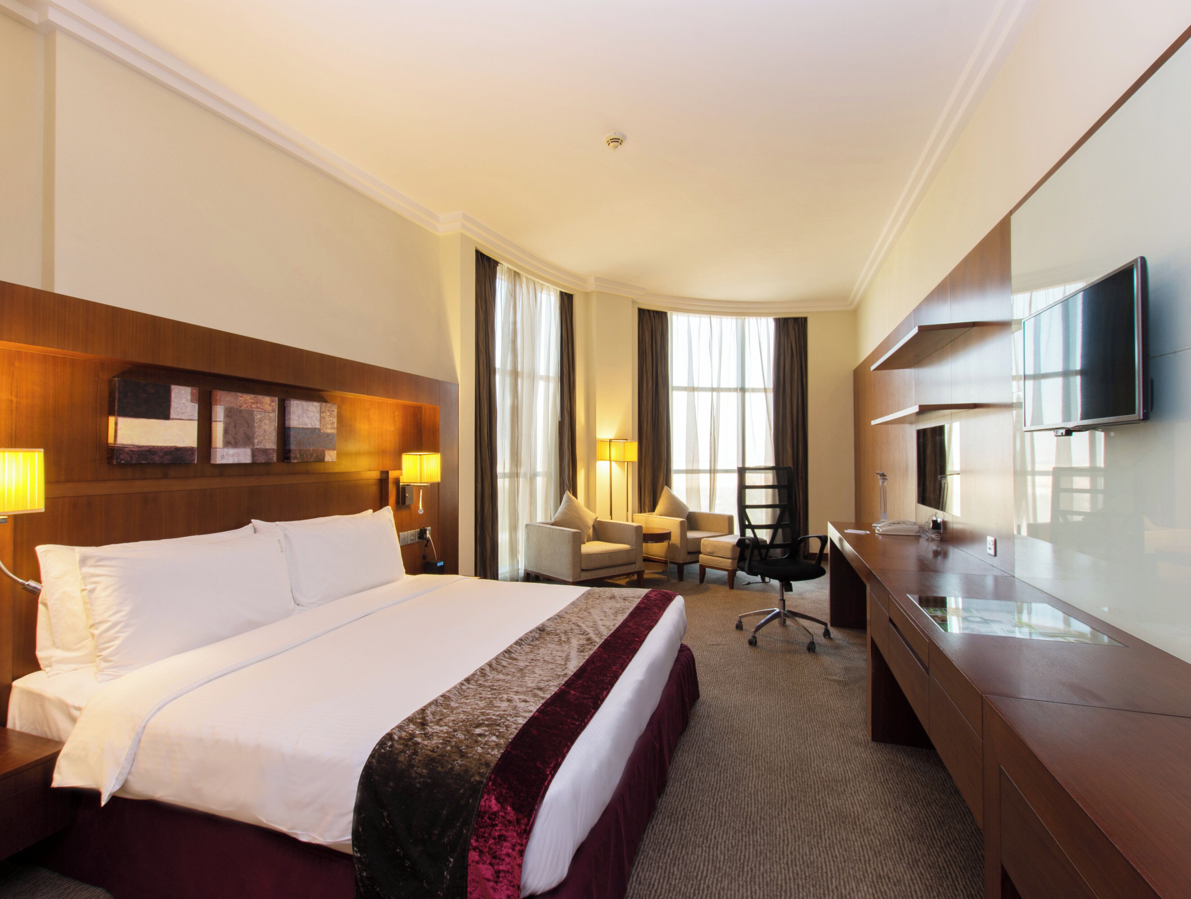 A hotel room with a large bed, a desk, a chair, a television, and a window with curtains.