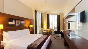 A hotel room with a large bed, a desk, a chair, a television, and a window with curtains.