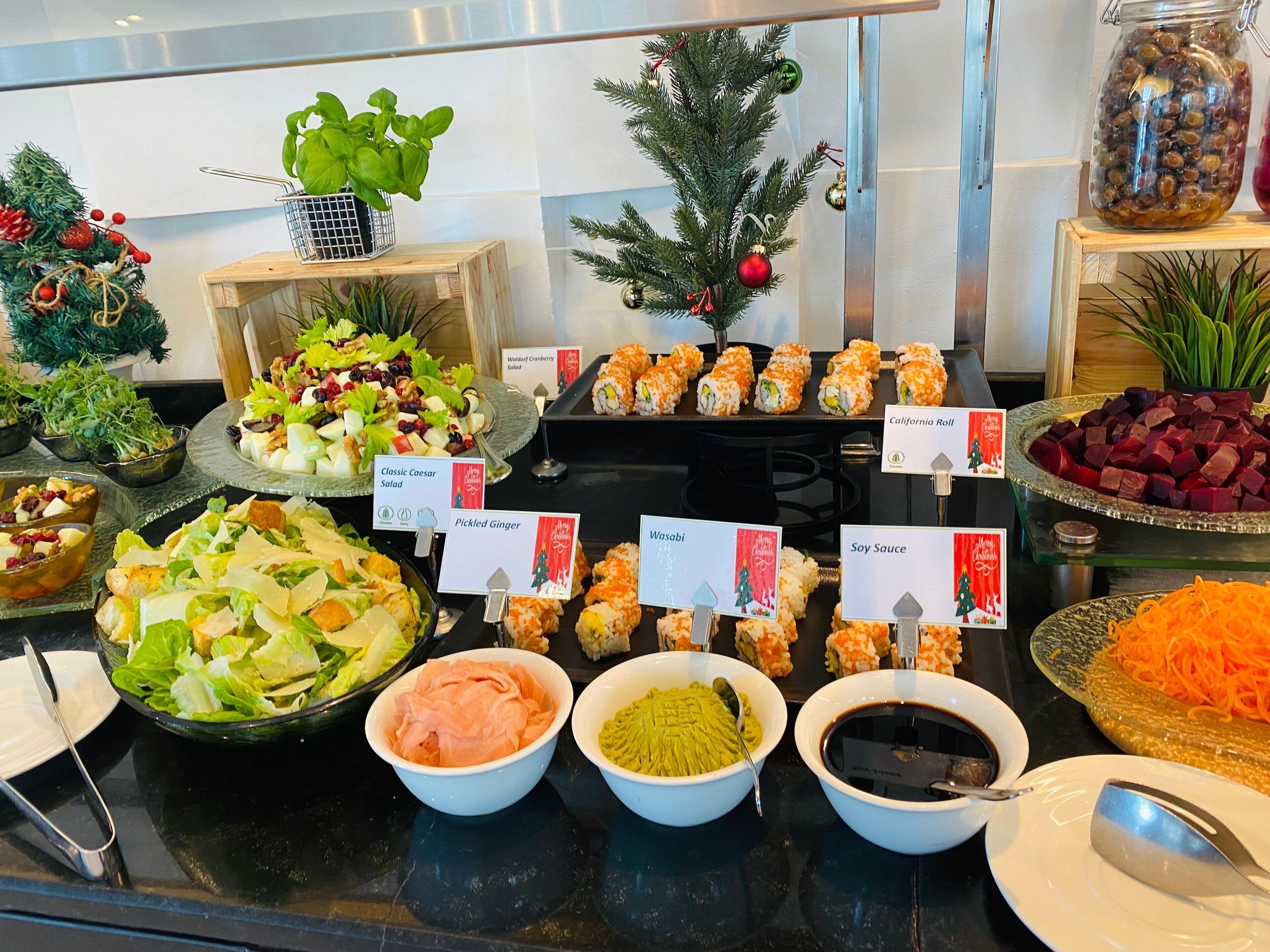 Un bufé con una variedad de platos, incluyendo ensaladas, sushi y salsas.