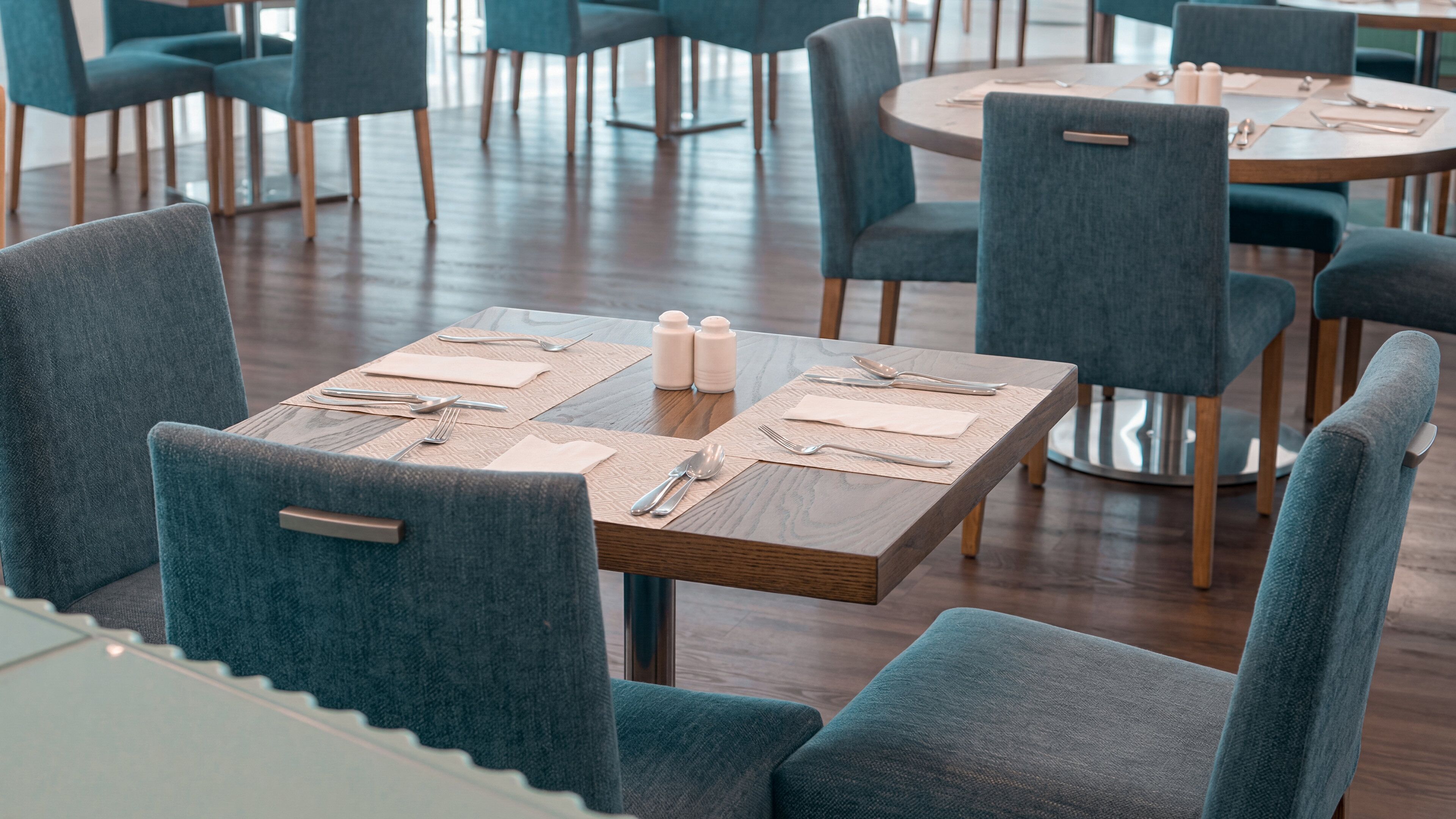 A dining area with tables set for two, chairs, and a wooden floor.