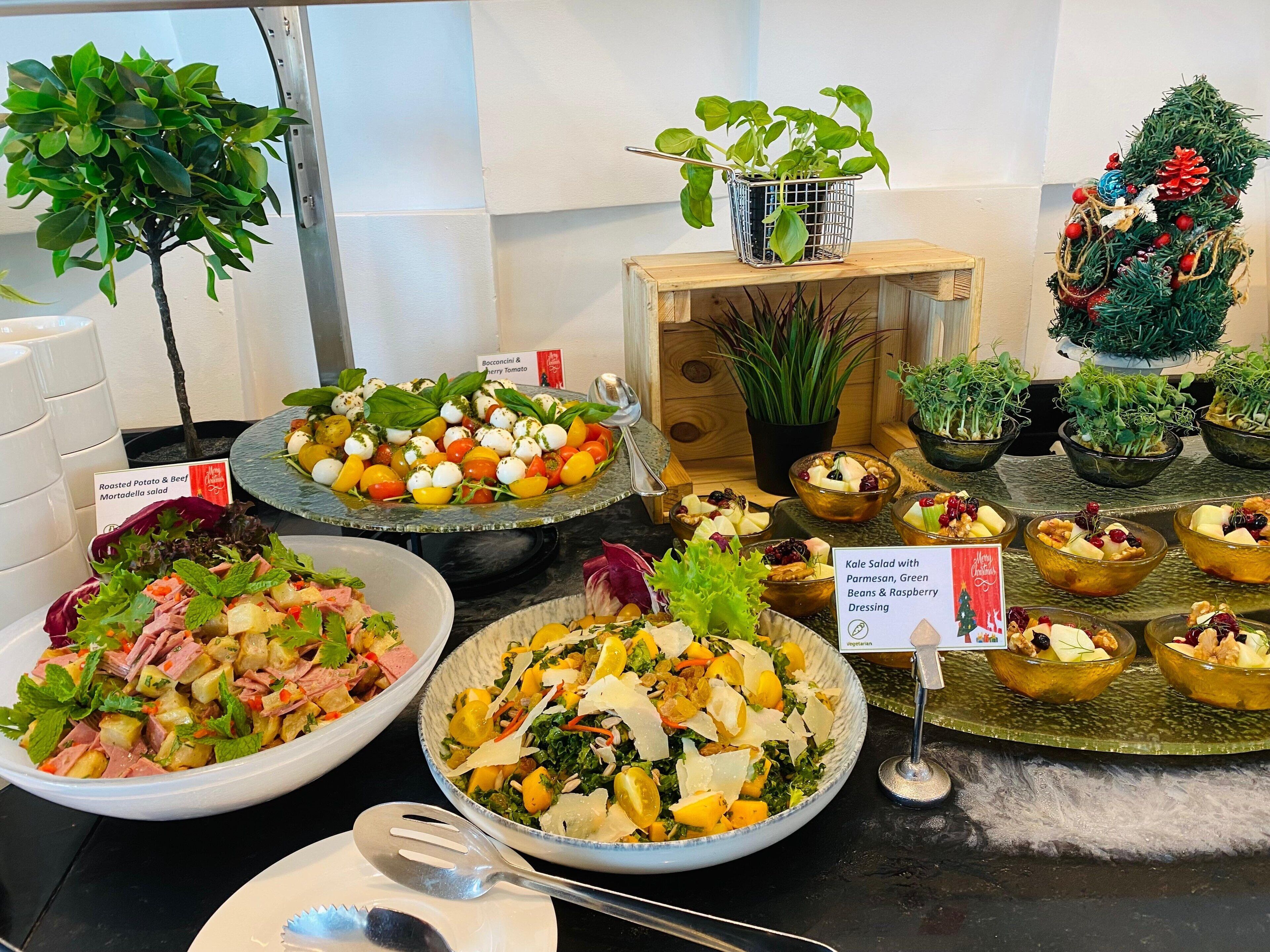 Ein reichhaltiges Buffet mit verschiedenen Salaten und Speisen, darunter ein Grünkohlsalat mit Parmesan, grünen Bohnen und Himbeer-Dressing.