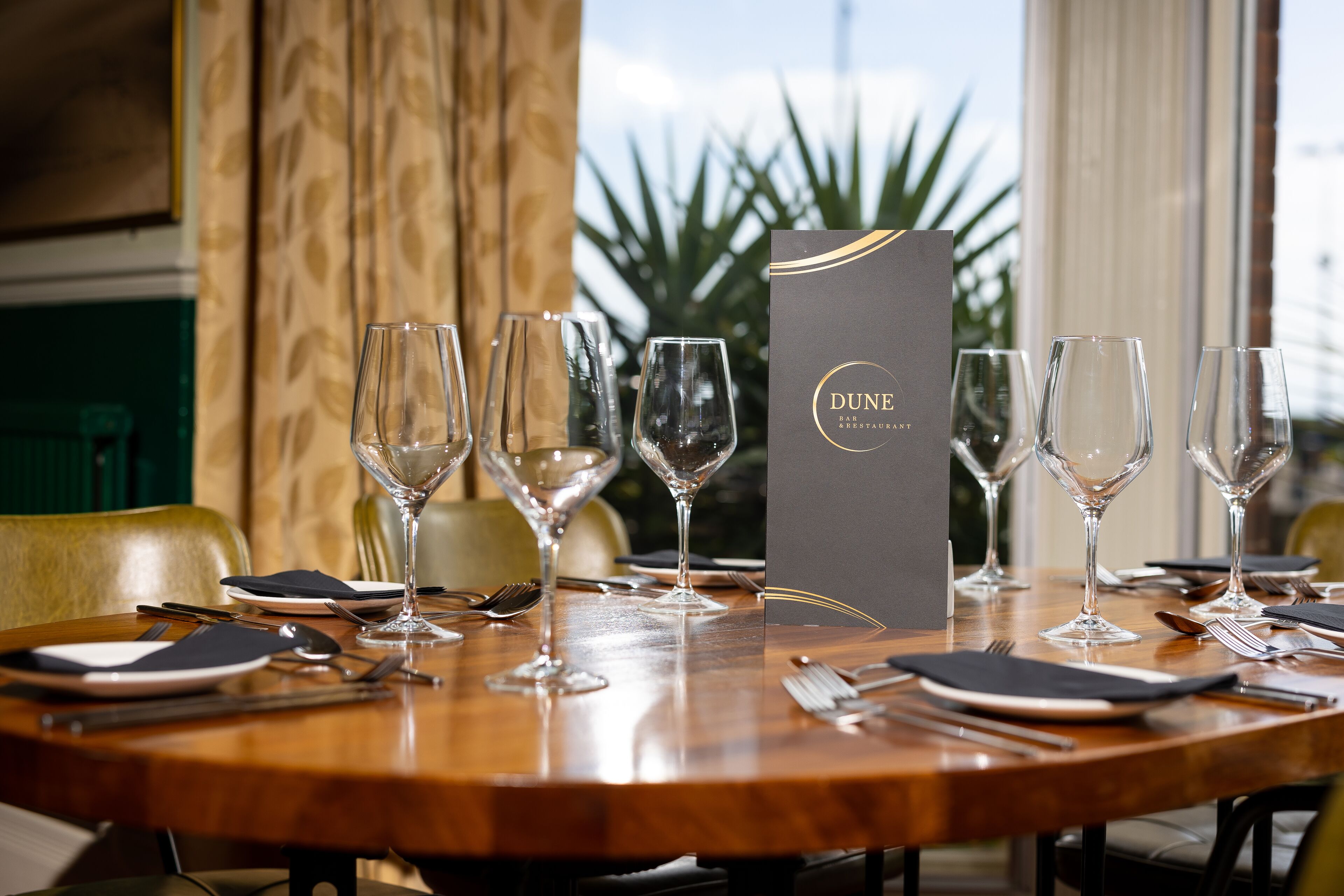 Une table à manger dressée avec des verres à vin, des assiettes, des couverts et un menu du restaurant Dune.