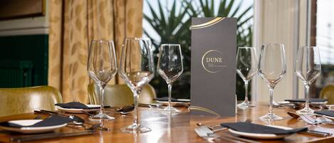A dining table set with wine glasses, plates, cutlery, and a menu for Dune Restaurant.