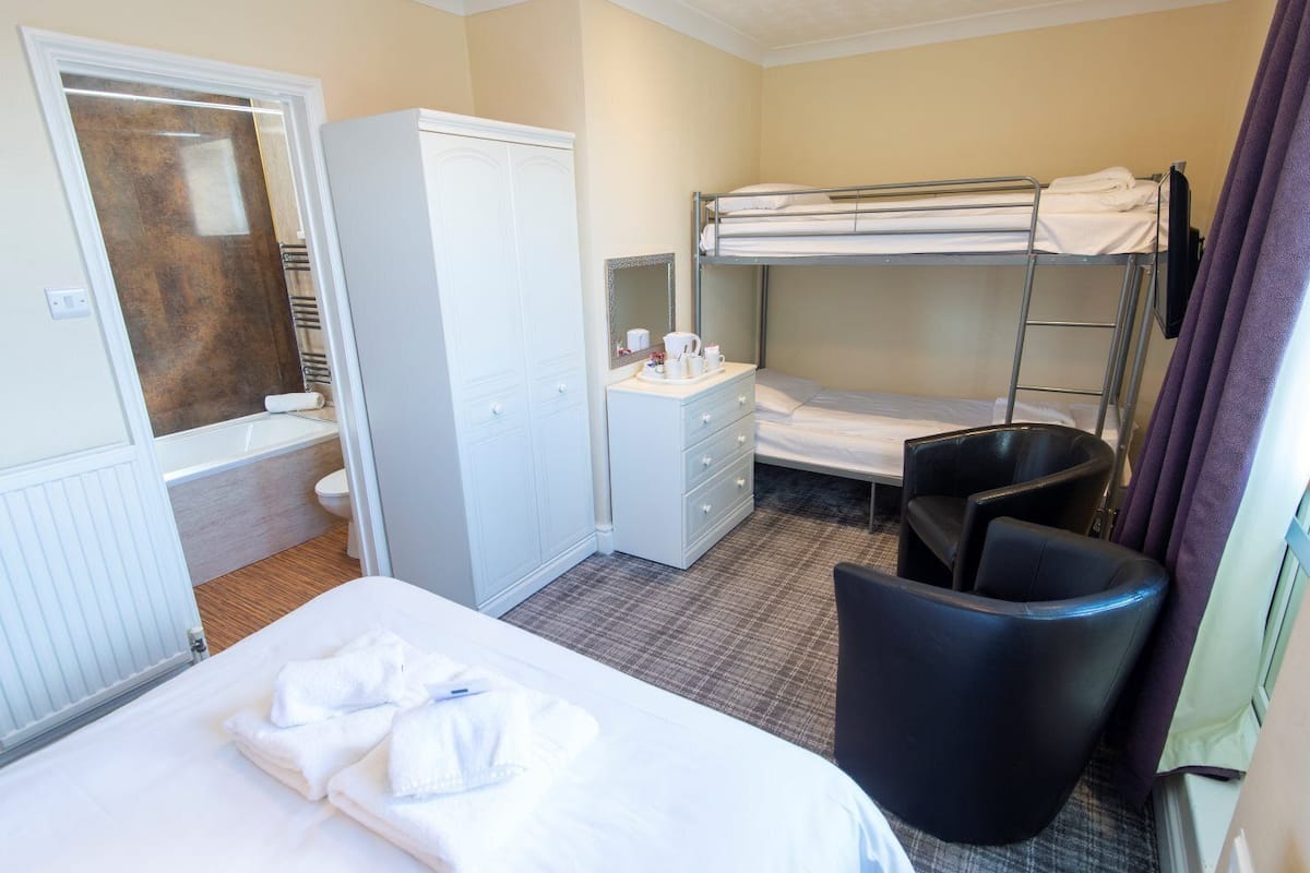 Una habitación de hotel con una cama, un escritorio con silla, un armario y una litera.