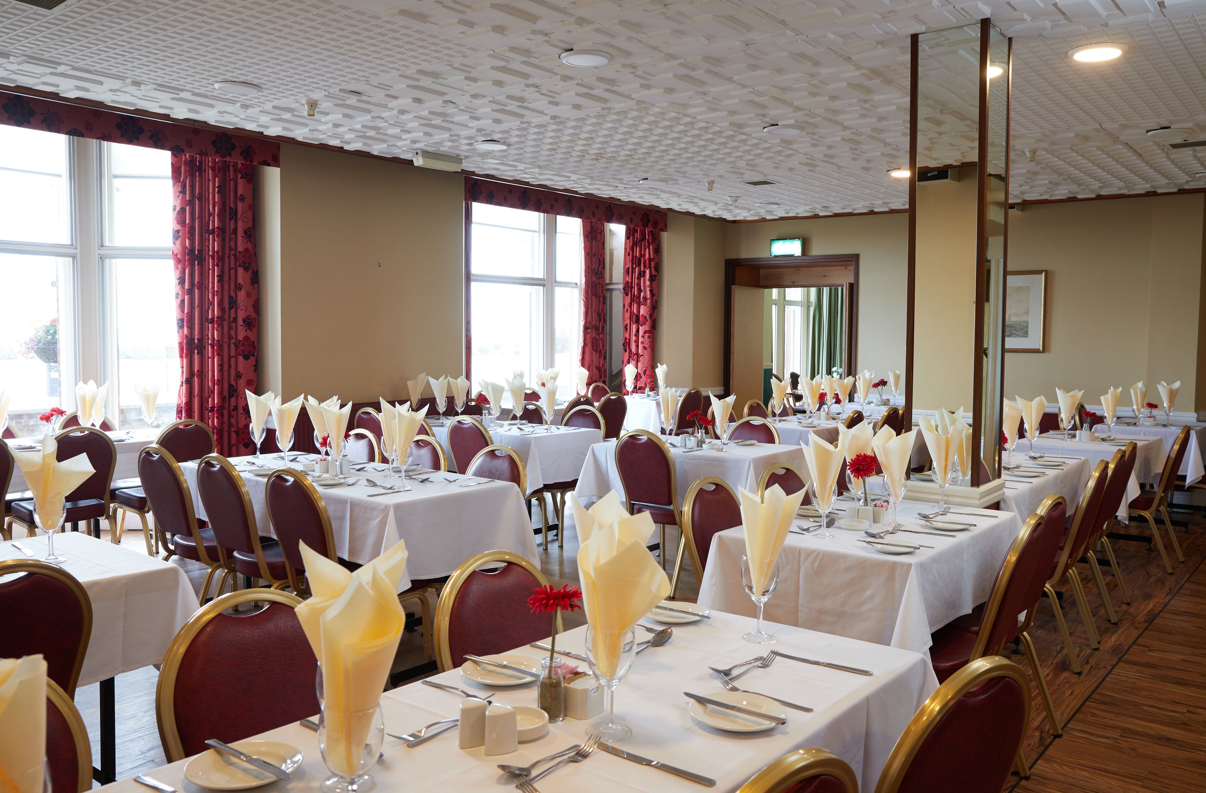 A banquet hall with multiple tables set for dining, featuring white tablecloths and gold chairs.