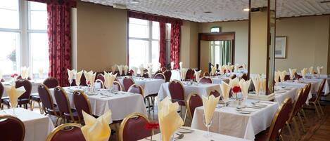 A banquet hall with multiple tables set for dining, featuring white tablecloths and gold chairs.