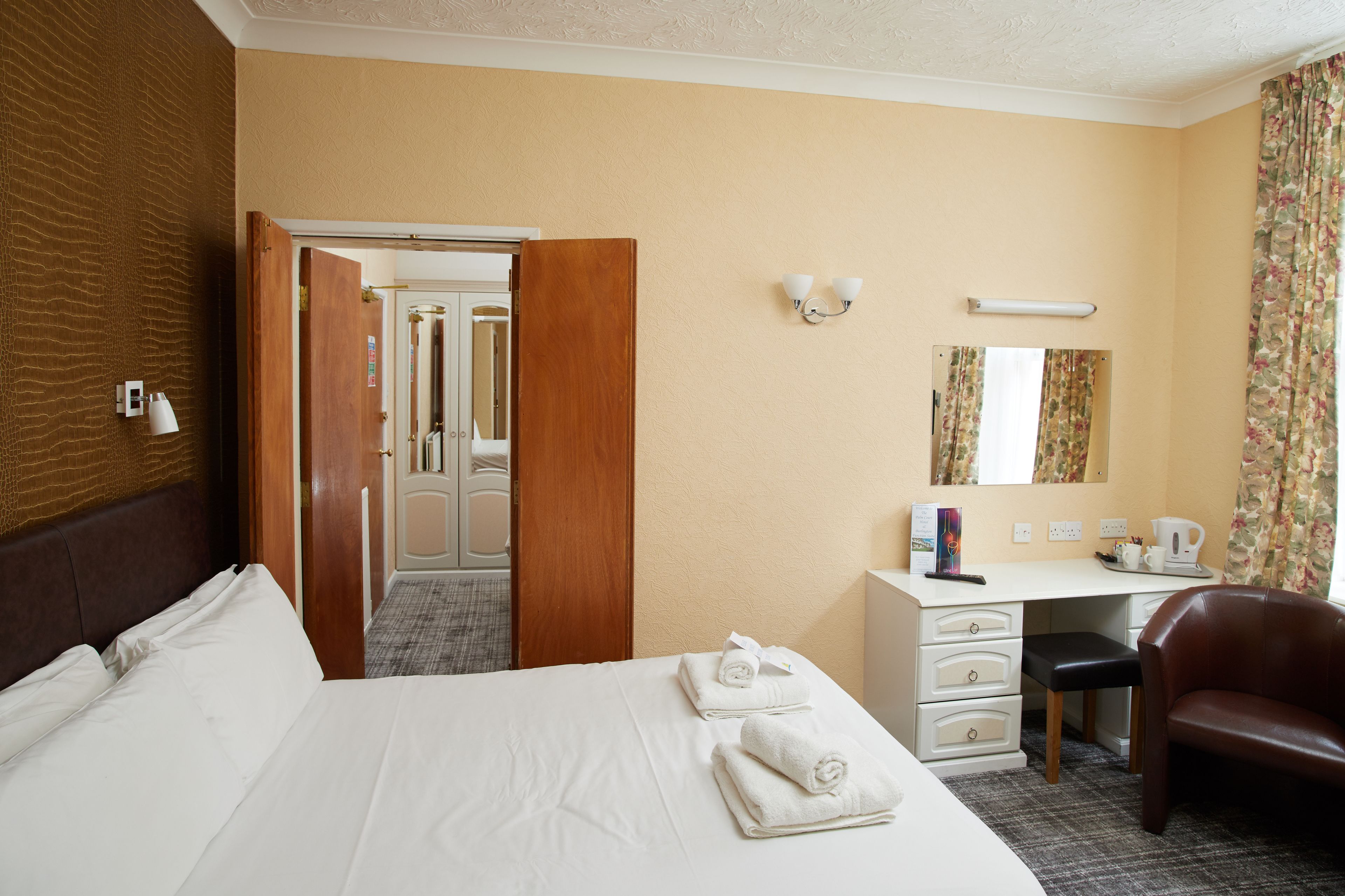 Ein Hotelzimmer mit Bett, Schreibtisch, Stuhl, Spiegel und einer Tür zu einem anderen Raum.