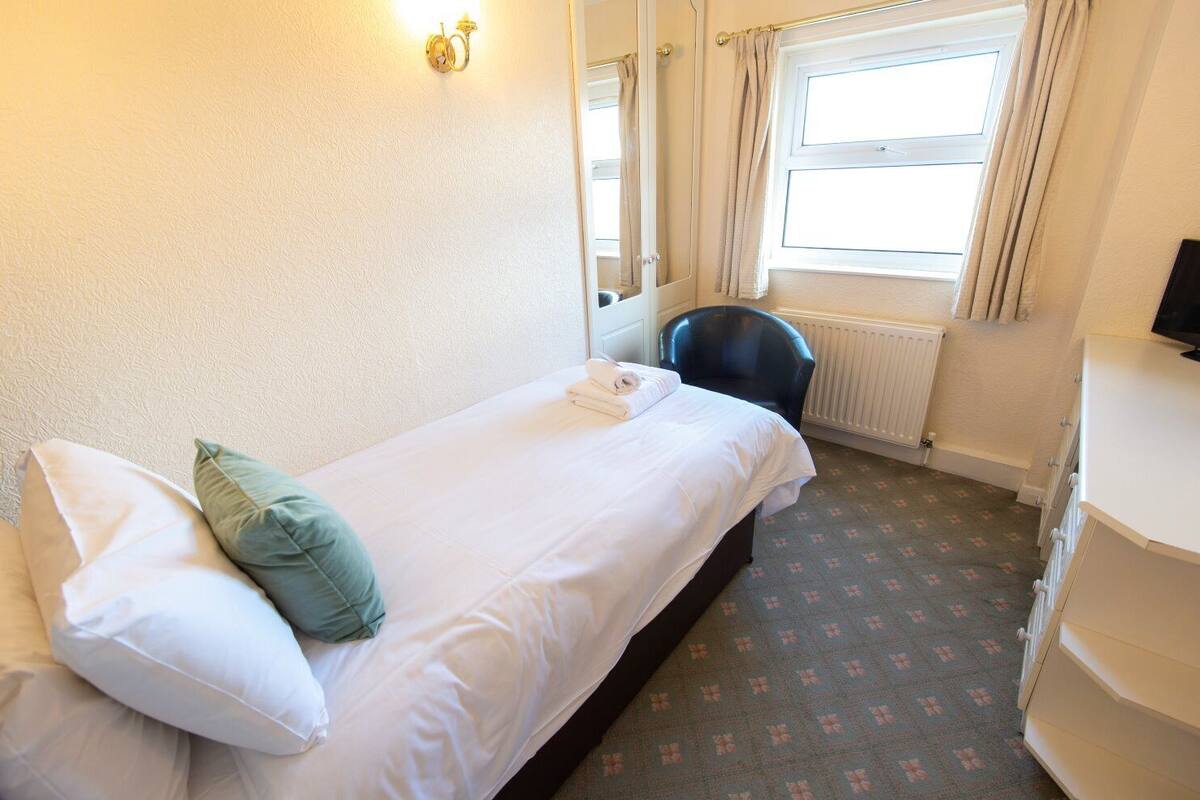 Ein Hotelzimmer mit einem Einzelbett, einem Sessel, einem Heizkörper und einem Fernseher.
