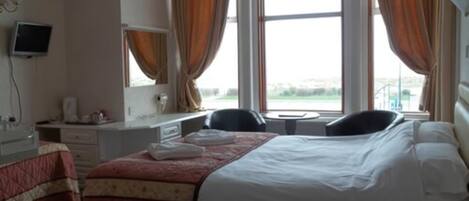 A hotel room with a bed, a desk, a chair, a television, and a window with curtains.