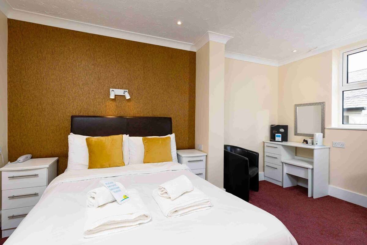 Ein Hotelzimmer mit Bett, Nachttischen, Schreibtisch, Stuhl, Spiegel und Fenster.