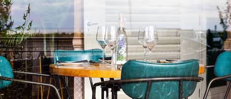 Un coin repas avec une table en bois, des chaises de couleur turquoise et une bouteille d’eau.