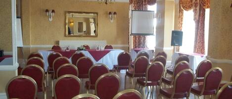 Une salle de conférence avec des rangées de chaises rouges, une table blanche, un écran de projection et un grand miroir au mur.