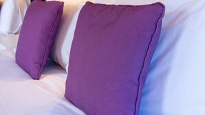A hotel room with a wooden textured wall, a black headboard, and white bedding with purple pillows. - The Palm Court Hotel (Great Yarmouth)