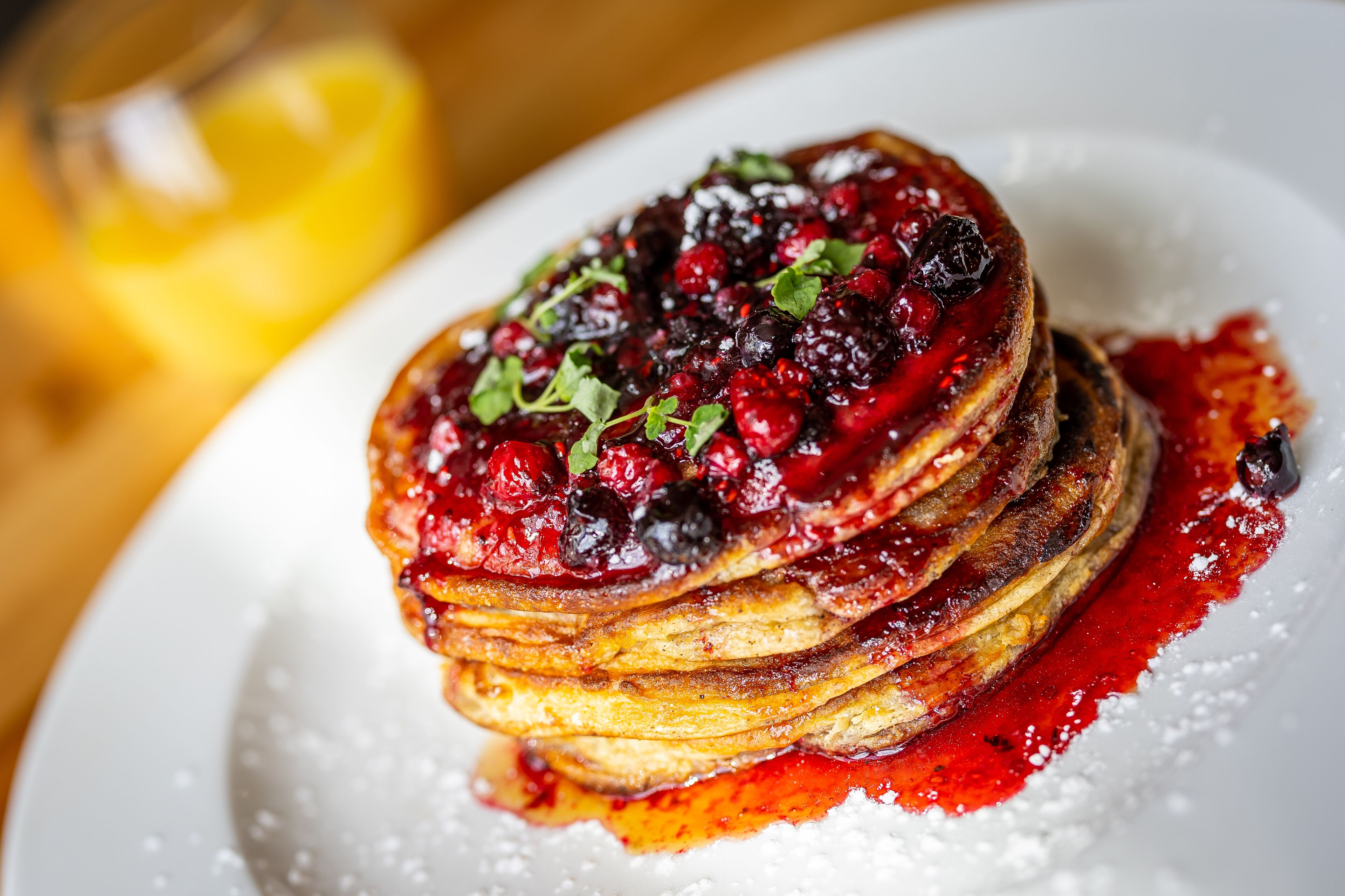 Een stapel pannenkoeken met bessencompote en poedersuiker op een wit bord.
