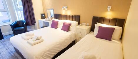 A hotel room with two beds, a desk, a chair, and a window with curtains.