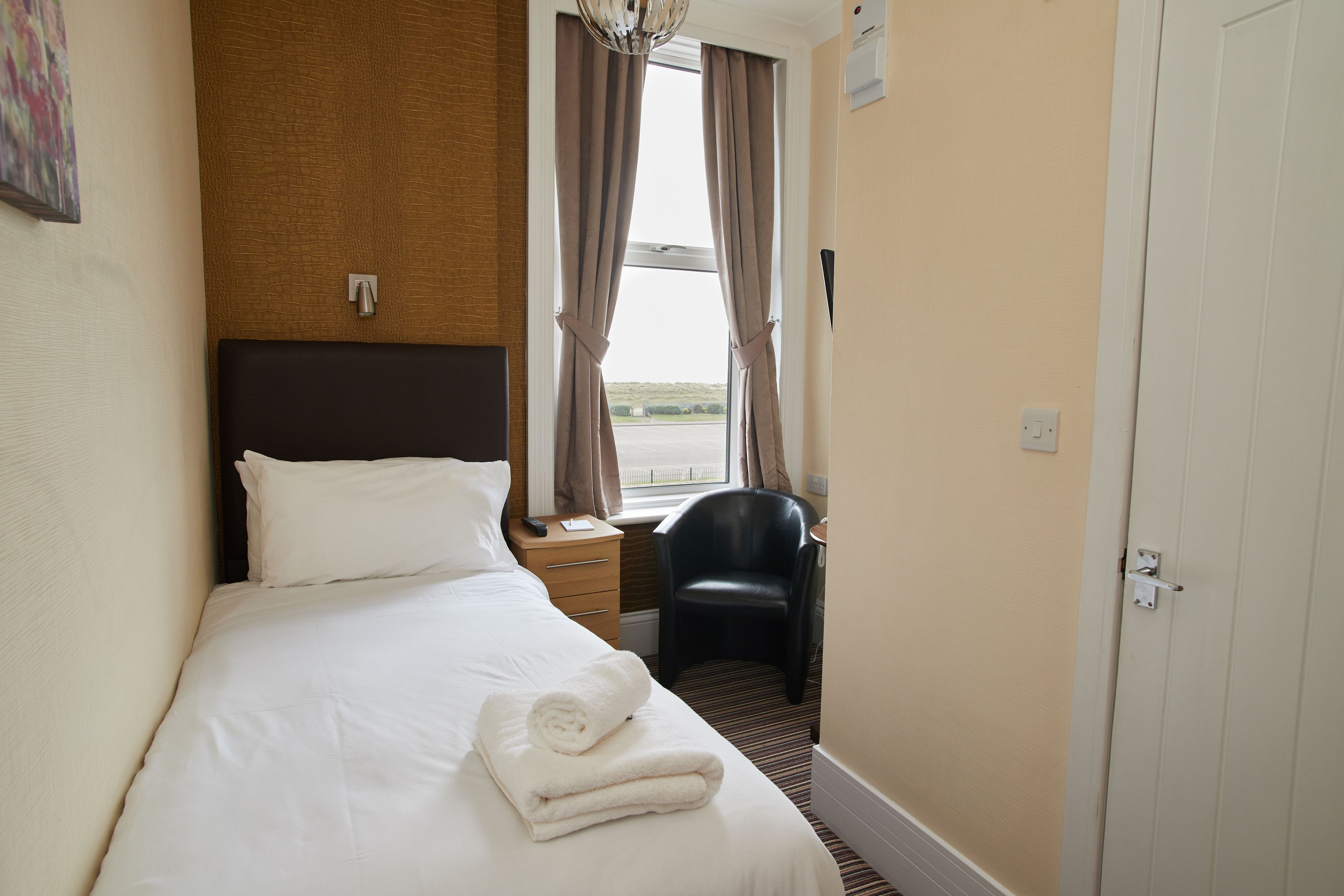 A hotel room with a bed, a chair, a nightstand, and a door.