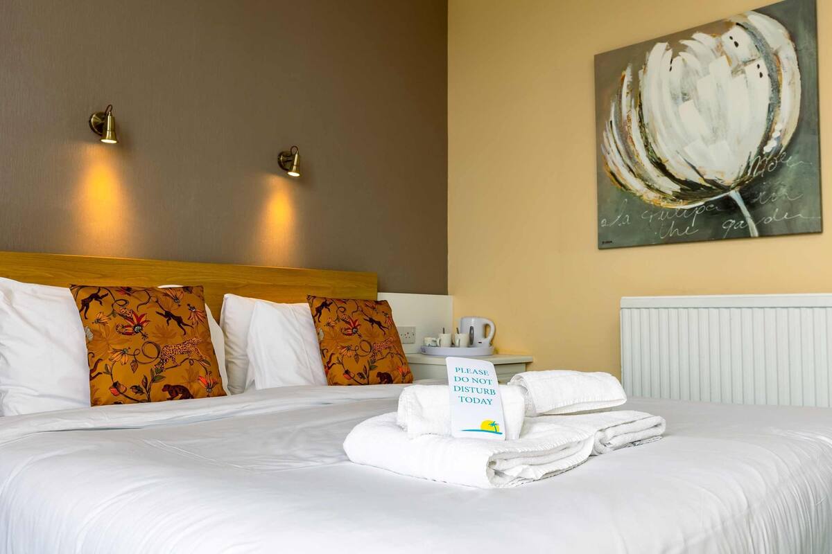 Ein Hotelzimmer mit einem ordentlich bezogenen Bett, zwei Wandleuchten, einem Gemälde und einem Schild auf dem Nachttisch.