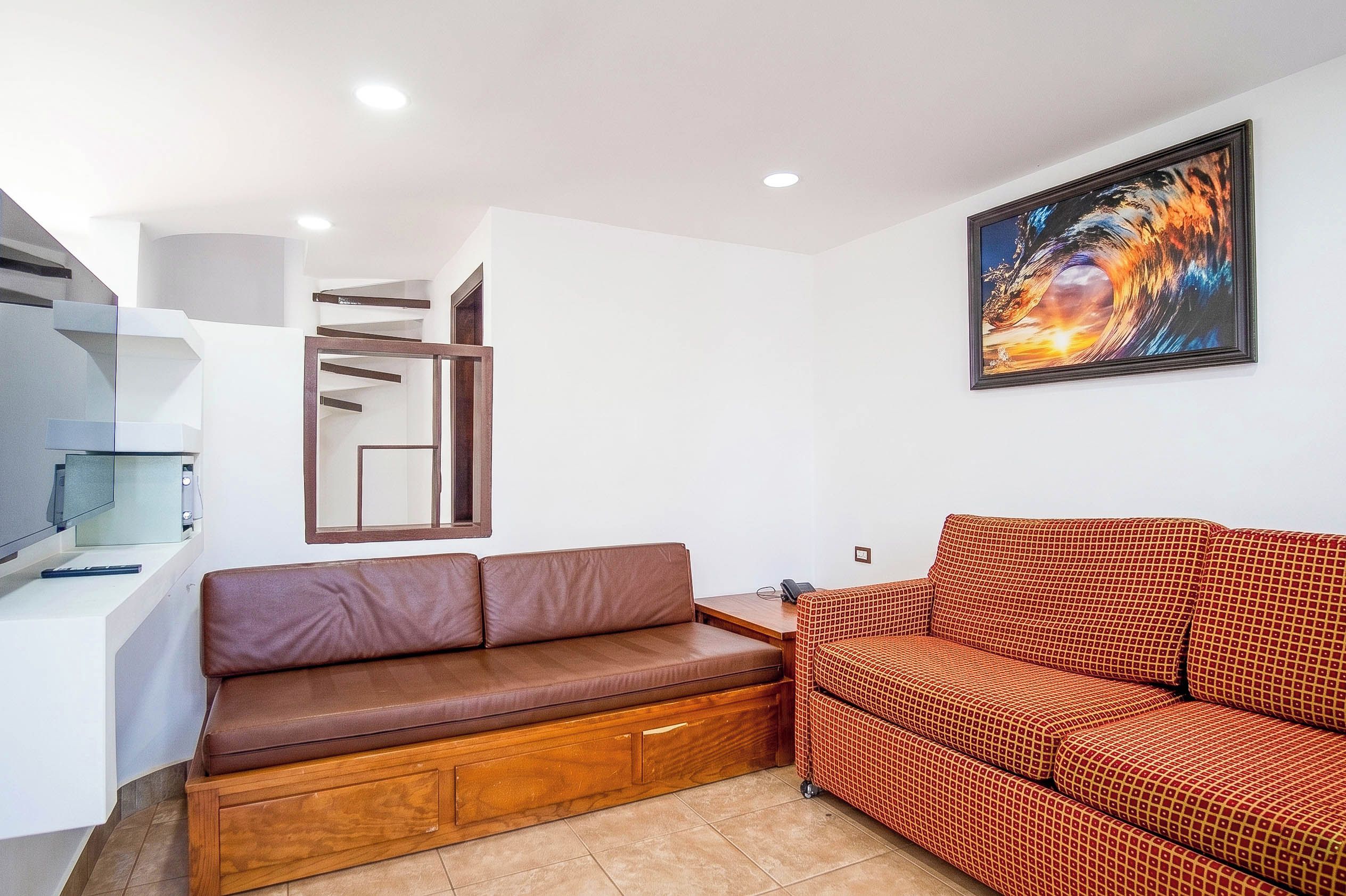 Ein modernes Wohnzimmer mit einem braunen Ledersofa, einem gemusterten roten Sofa, einem Holzschrank und einem gerahmten Kunstwerk an der Wand.