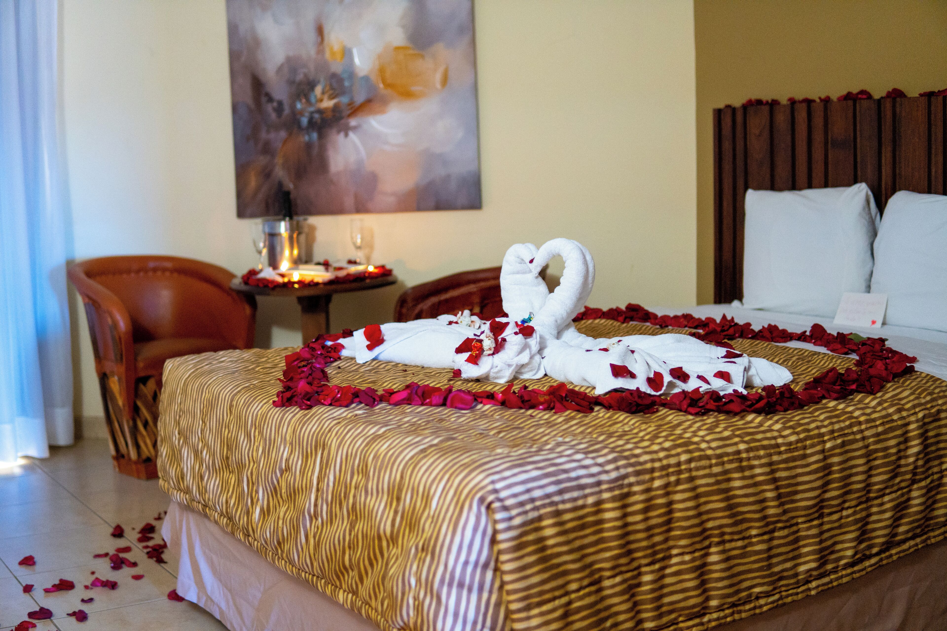 A hotel room with a bed adorned with rose petals and a towel swan centerpiece.