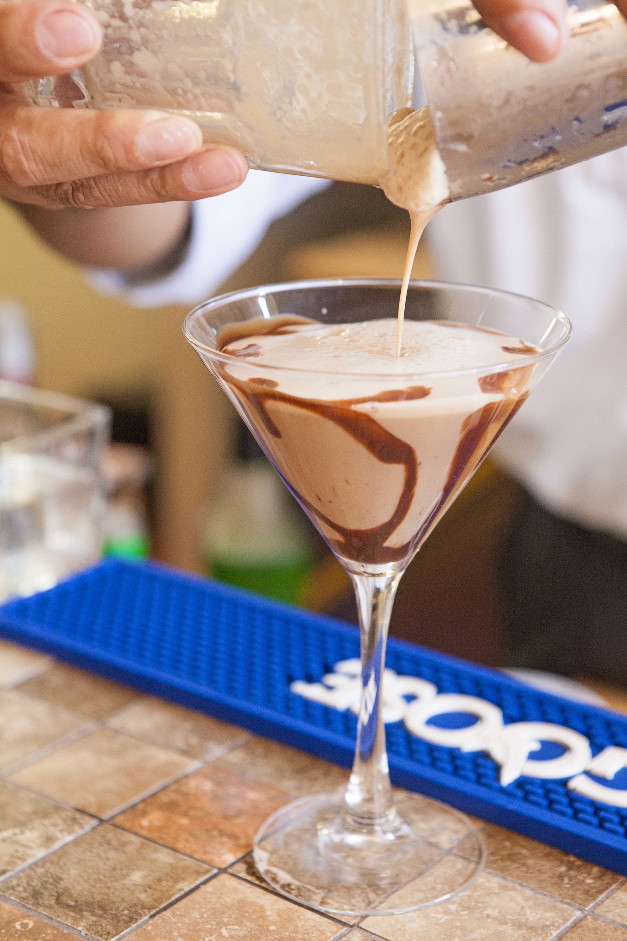 A martini glass being filled with a chocolate drink.