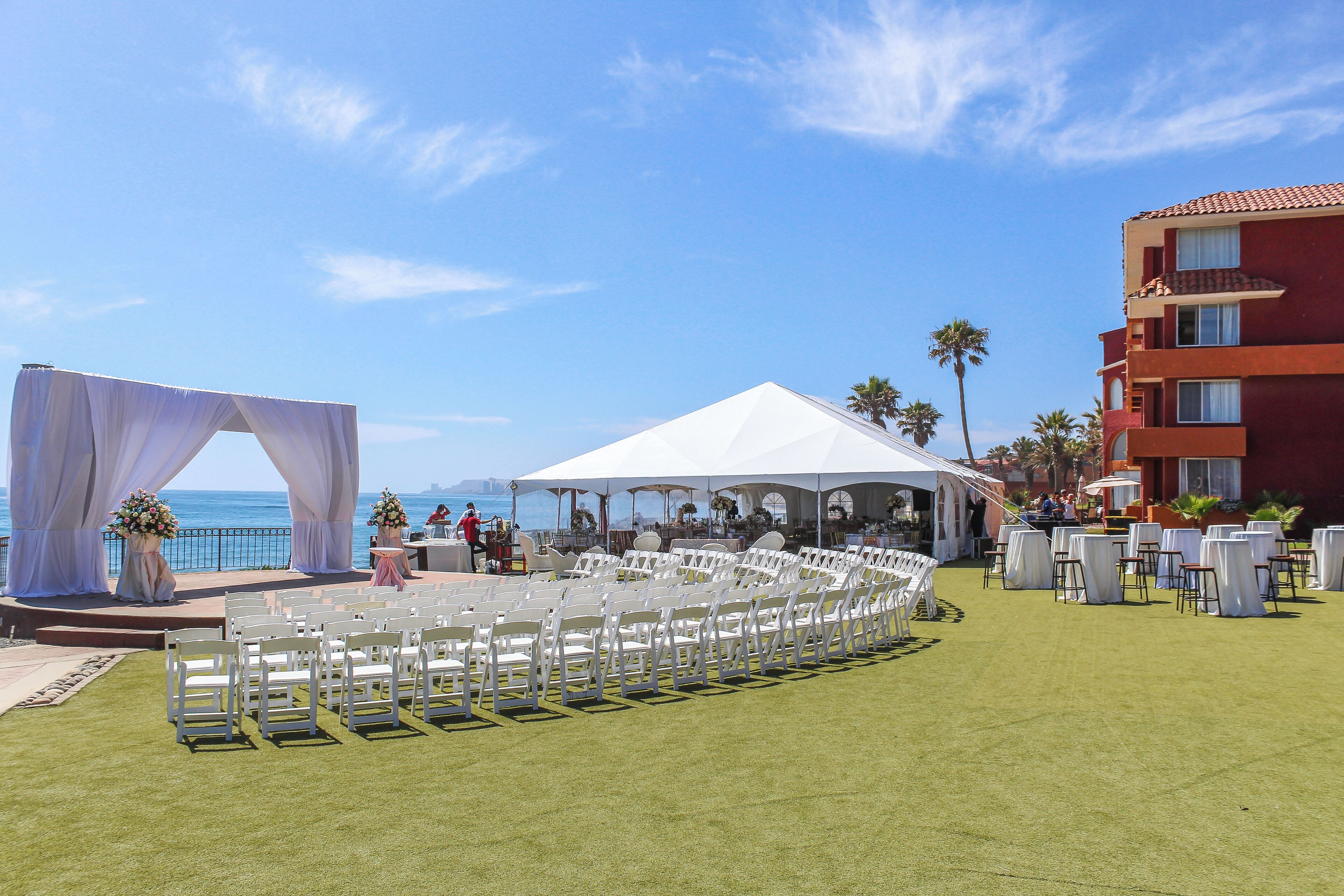 Un lieu de réception en plein air pour les mariages, doté d’une scène, de chaises blanches et de tables disposées sur une pelouse.
