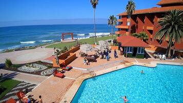 Relax by the ocean-view pool surrounded by a patio with lounge chairs and umbrellas, and a landscaped garden with palm trees.