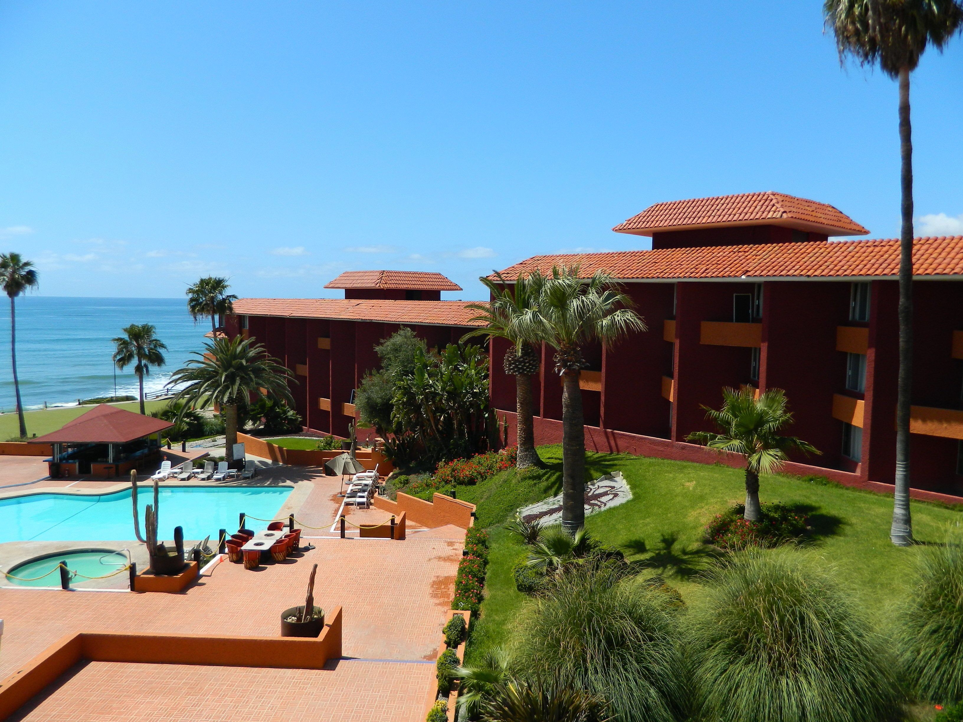 A resort with a swimming pool, palm trees, and a view of the ocean.