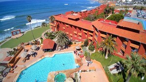 Un hotel con piscina, palmeras y vista al océano.
