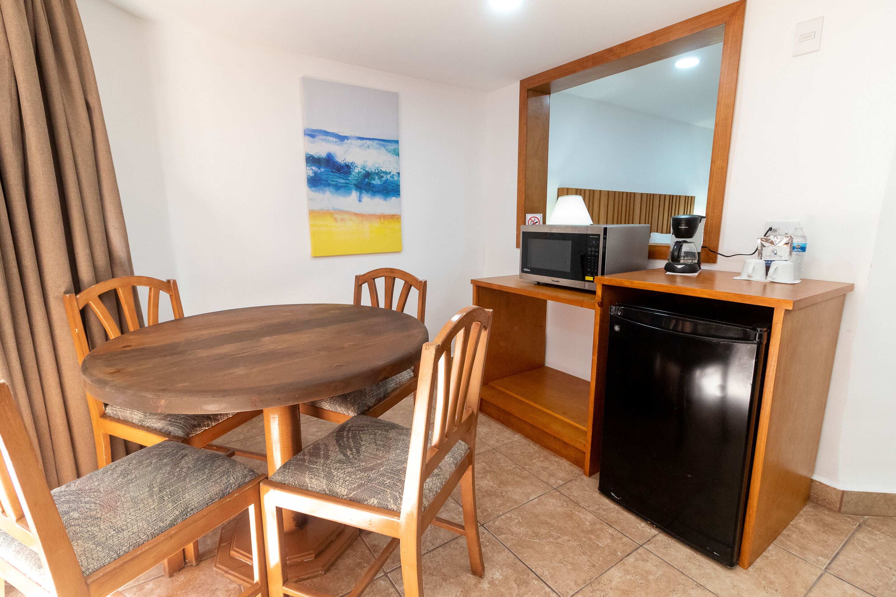 A compact kitchen with a wooden dining table, chairs, a microwave, a coffee maker, and a refrigerator.