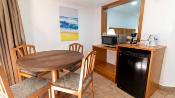 A compact kitchen with a wooden dining table, chairs, a microwave, a coffee maker, and a refrigerator.