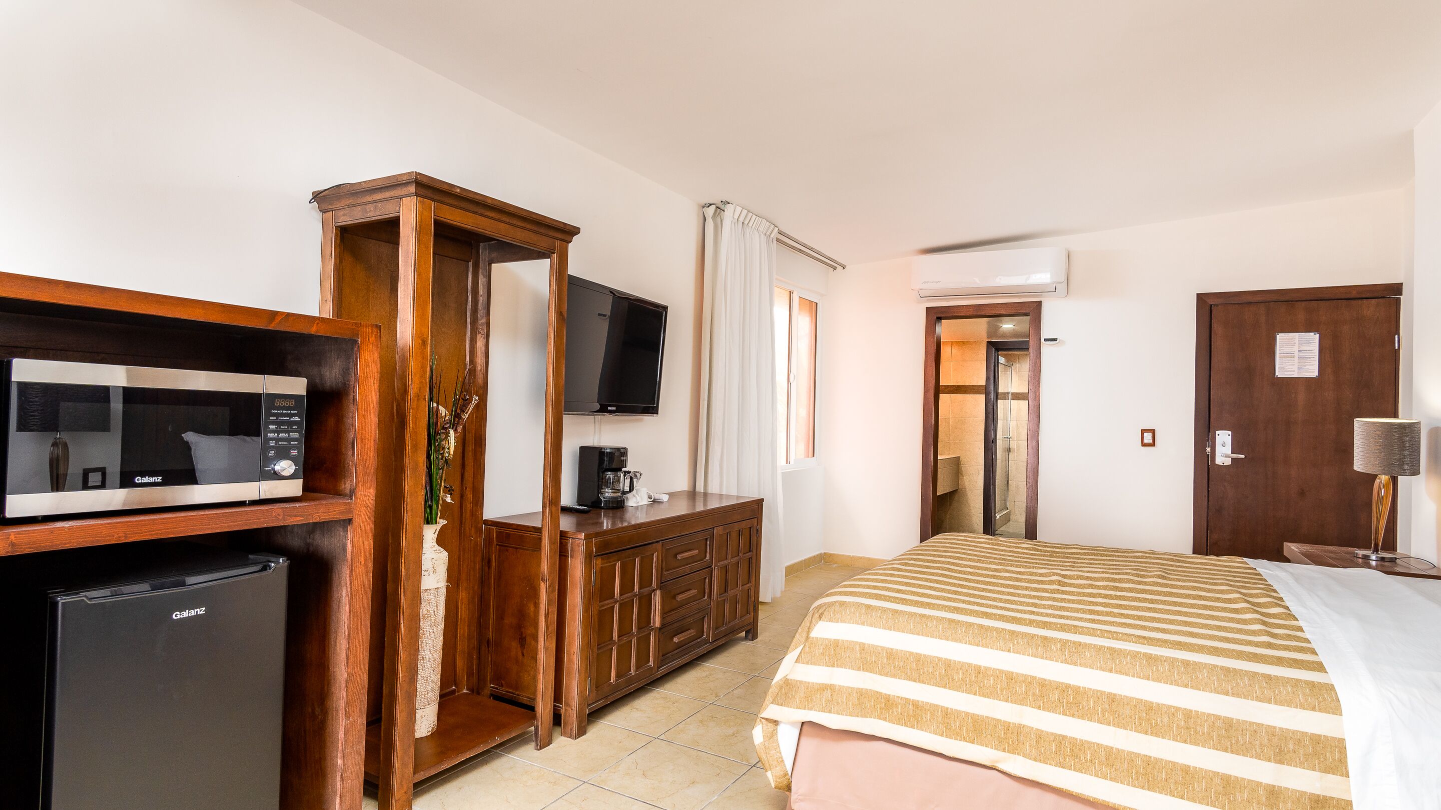 Una habitación de hotel con cama, armario de madera, minibar, televisor y puerta de baño.